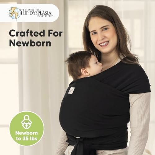 Woman holding baby in a black wrap carrier, promoting hip dysplasia awareness.