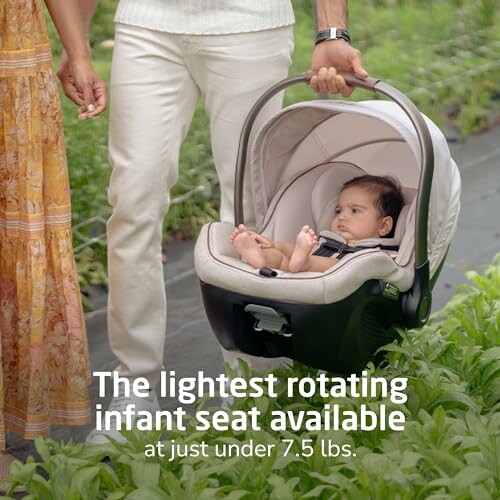 Person carrying infant in a rotating car seat outdoors.