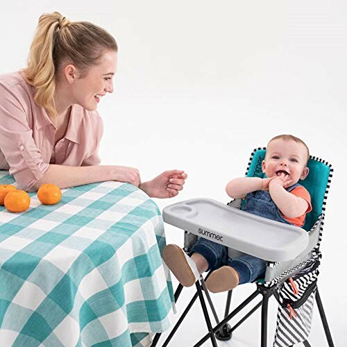 Mother smiling at baby in a portable high chair at a table with oranges.