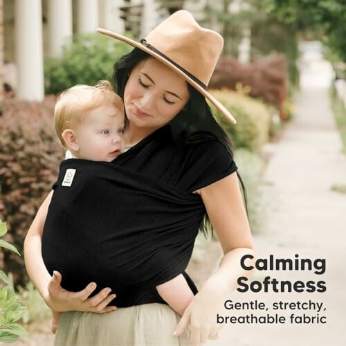 Mother carrying baby in a black wrap, outdoors.